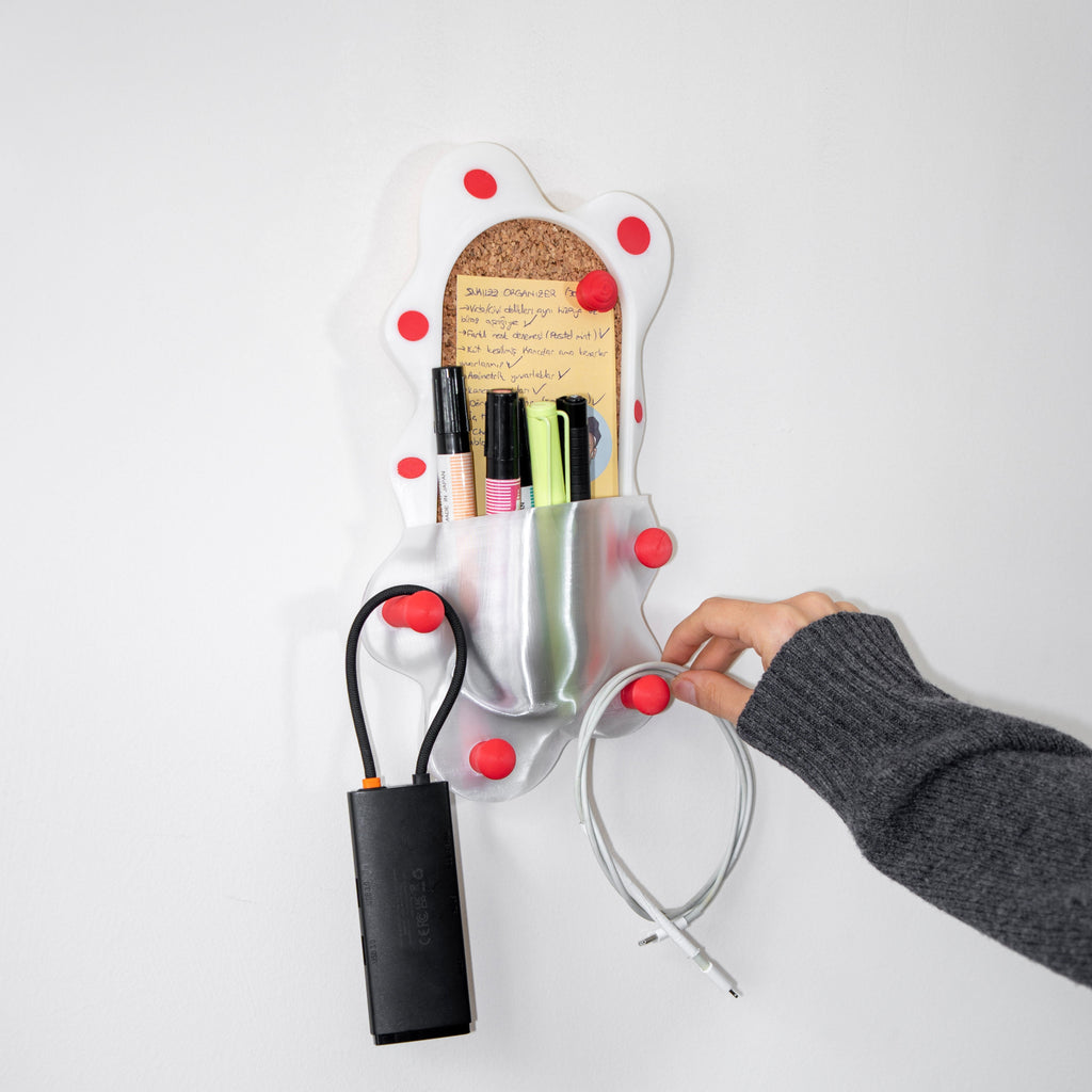 Wall-mounted organizer with red knobs holding stationery items on a white background