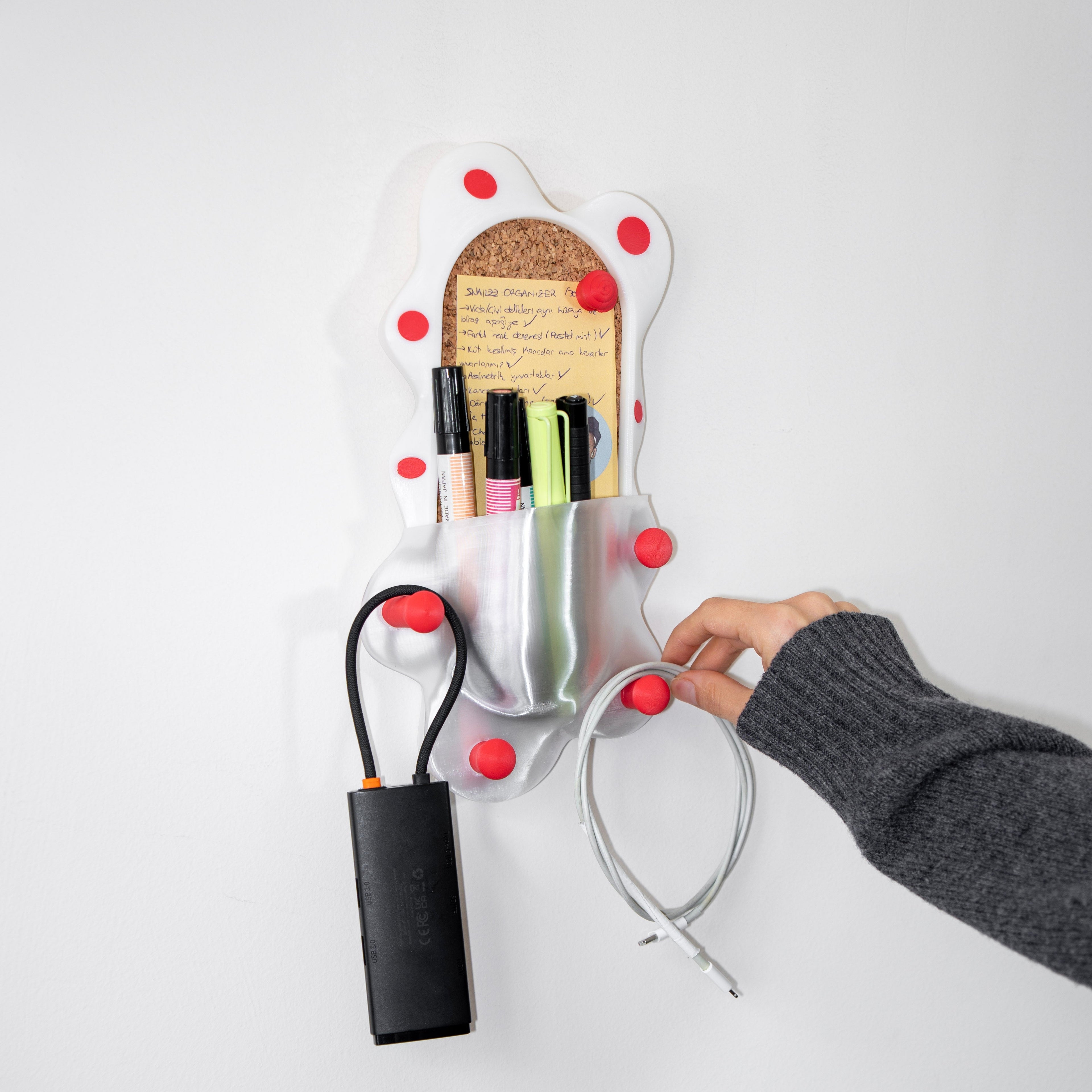 Wall-mounted organizer with red knobs holding stationery items on a white background