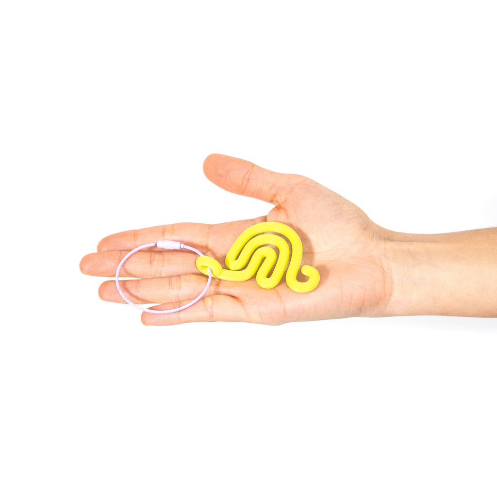 Hand holding a lime green snail shaped charm with a white background