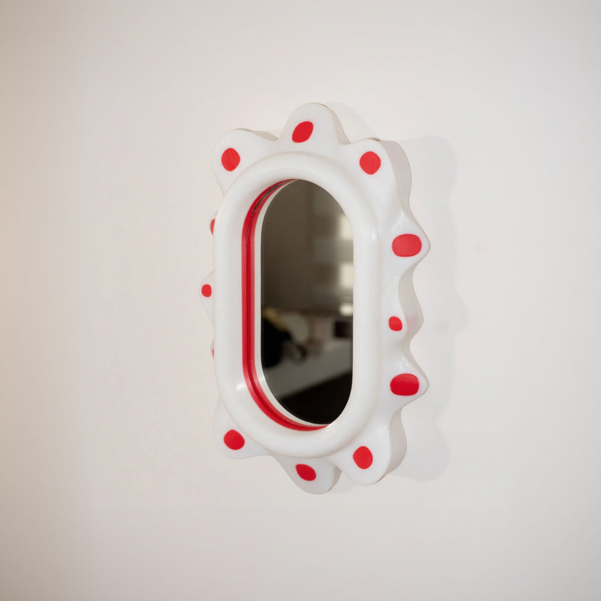 Small oval mirror with red polka dots on a white background