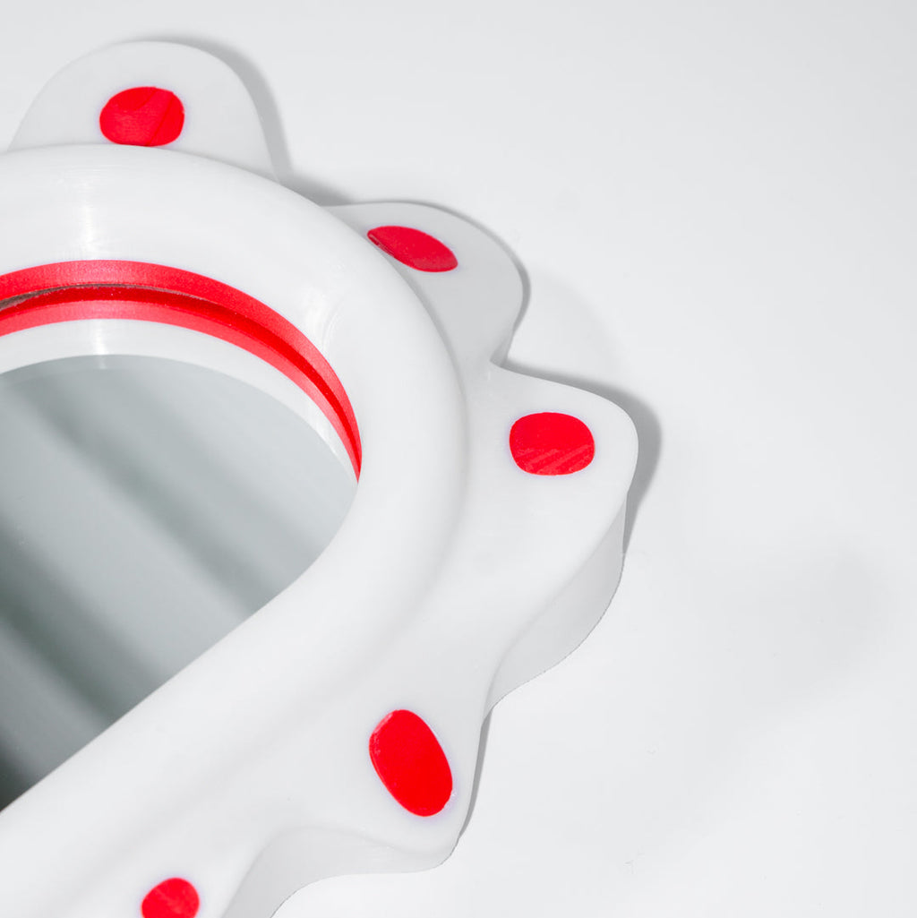 Close up of a decorative mirror inspired by sea slugs with red polka dots on a white background