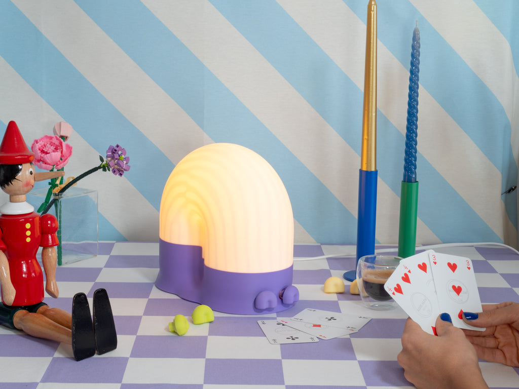 Snail lamp on a checkered tablecloth with playing cards and candles in the background
