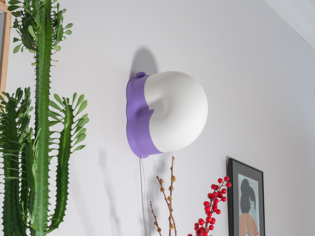 White and purple snail inspired lampshade on a white wall with plants and a modern decor.