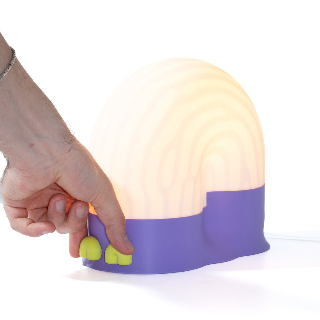 Hand holding a small lamp with a purple base and green accents on a white background