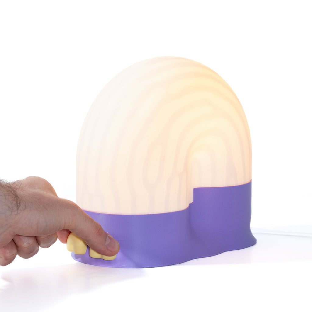 Hand holding a round, purple and white lamp on a white background